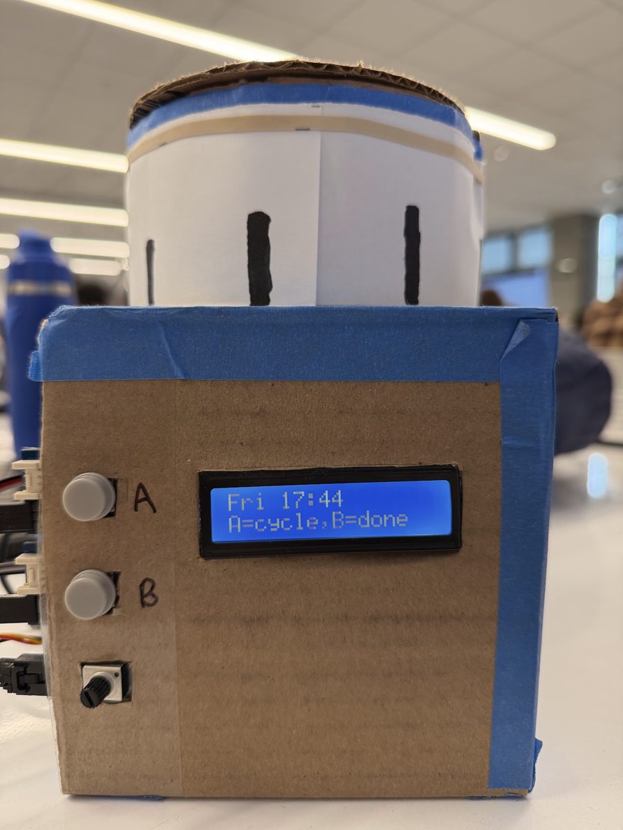 A cardboard box with two buttons and a blue LCD reading Fri 17:44, A=cycle, B=done